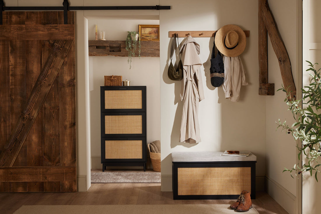 Black rattan shoe cabinet and storage bench with wall hooks, coats and bags in a warm neutral hallway.