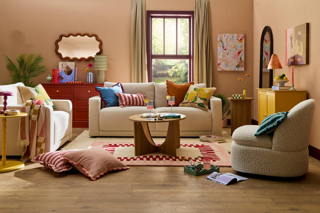 Palm Springs Pop living room with cream sofa and armchair, colourful cushions, scalloped rug, warm peach walls and playful décor.