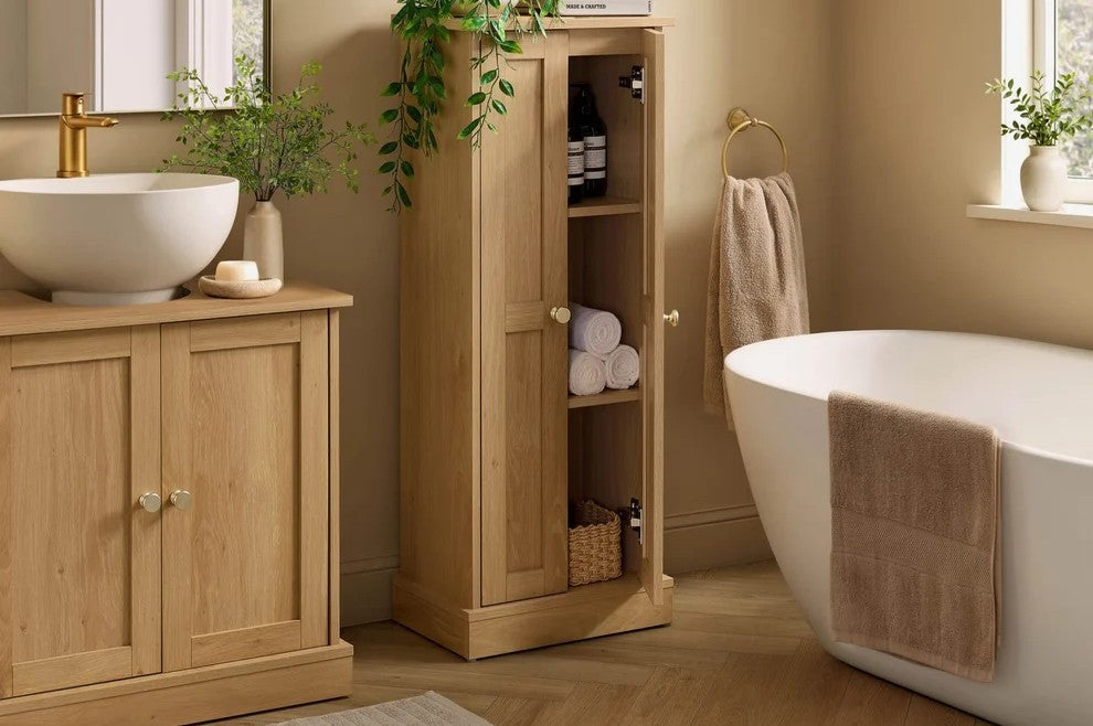 Light wood under sink bathroom cabinet and tall bathroom storage cabinet styled beside a freestanding bath.